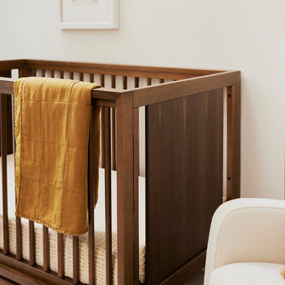 Babyletto's Peggy 3-in-1 Convertible Crib with blanket over the right side of the rail  in -- Color_Natural Walnut