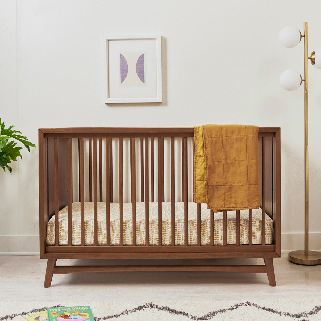 Front view of Babyletto's Peggy 3-in-1 Convertible Crib with blanket over the rail  in -- Color_Natural Walnut