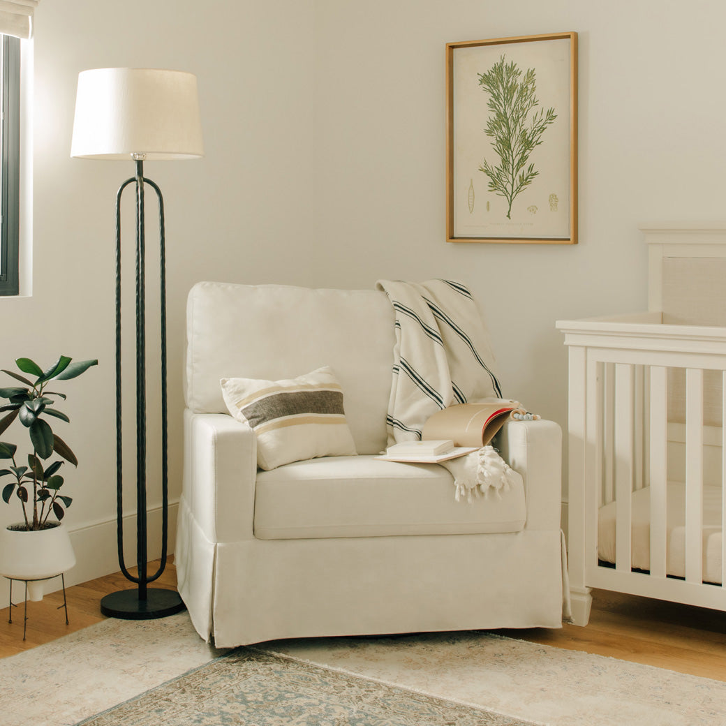 The Namesake's Crawford Pillowback Chair-And-A-Half Comfort Swivel Glider next to a lamp and crib in -- Color_Performance Cream Eco-Weave