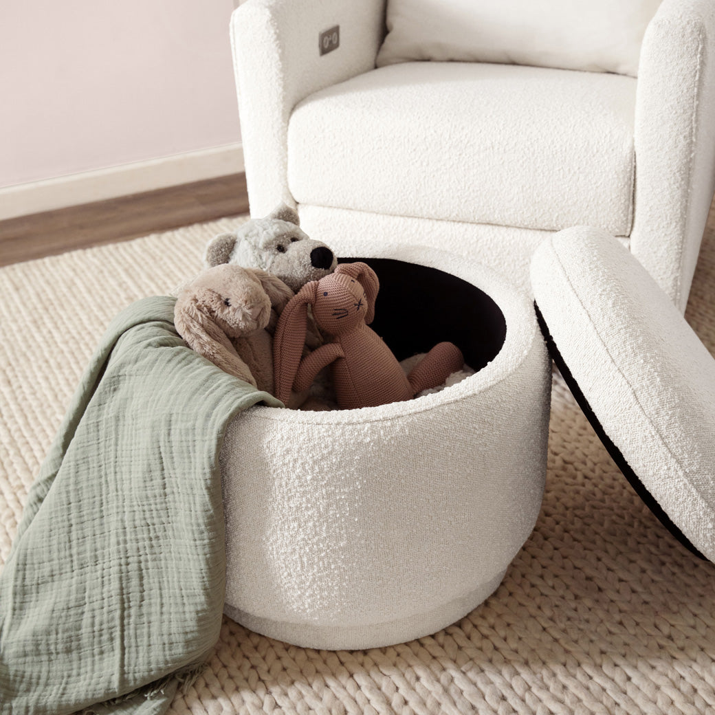 The Babyletto Enoki Storage Ottoman with the top off with a blanket and toys in it, lifestyle image in --Color_Ivory Boucle