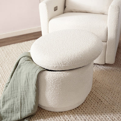 The Babyletto Enoki Storage Ottoman with the top slightly angled and with a blanket in it, lifestyle image in --Color_Ivory Boucle