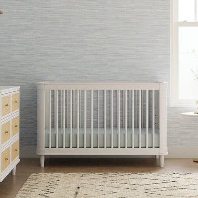 Front view of The Namesake Marin 3-in-1 Convertible Crib next to dresser in -- Color_Warm White/Honey Cane