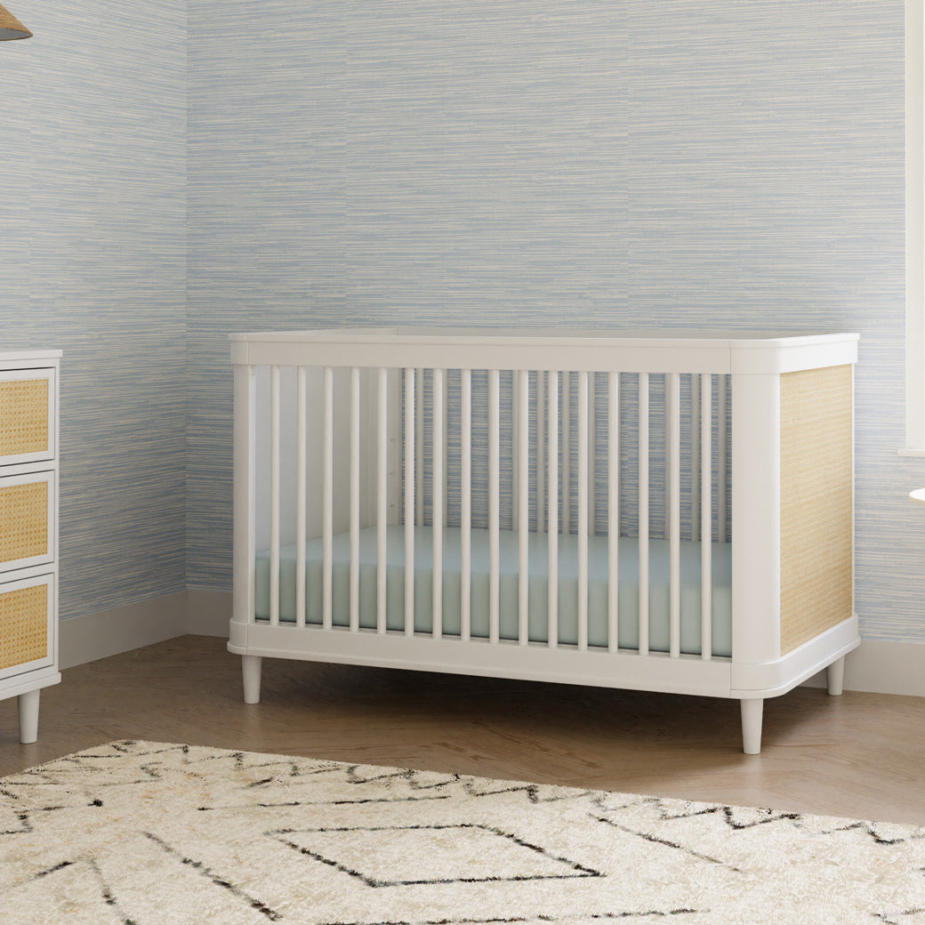 The Namesake Marin 3-in-1 Convertible Crib next to dresser in -- Color_Warm White/Honey Cane