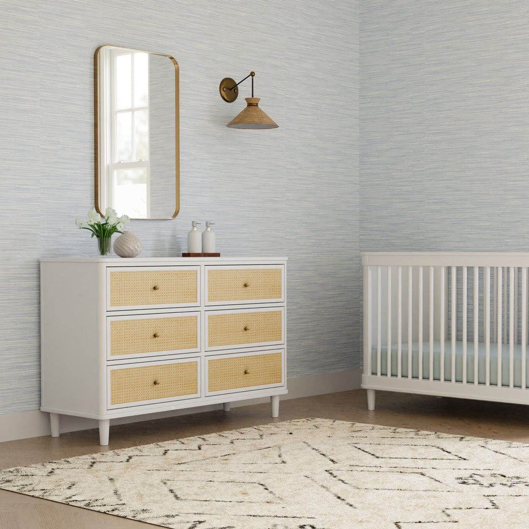 Namesake's Marin 6 Drawer Dresser under a mirror next to a crib in -- Color_Warm White/Honey Cane