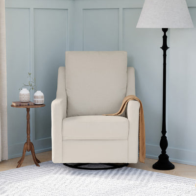 Lifestyle front view of The DaVinci Field Swivel Glider next to a table and lamp in --Color_Cotton Weave