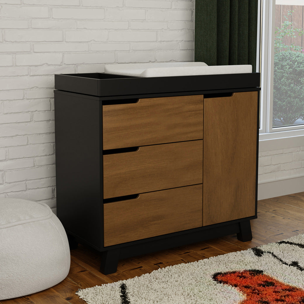Lifestyle side view of The Babyletto Hudson Changer Dresser next to window in -- Color_Black/Natural Walnut