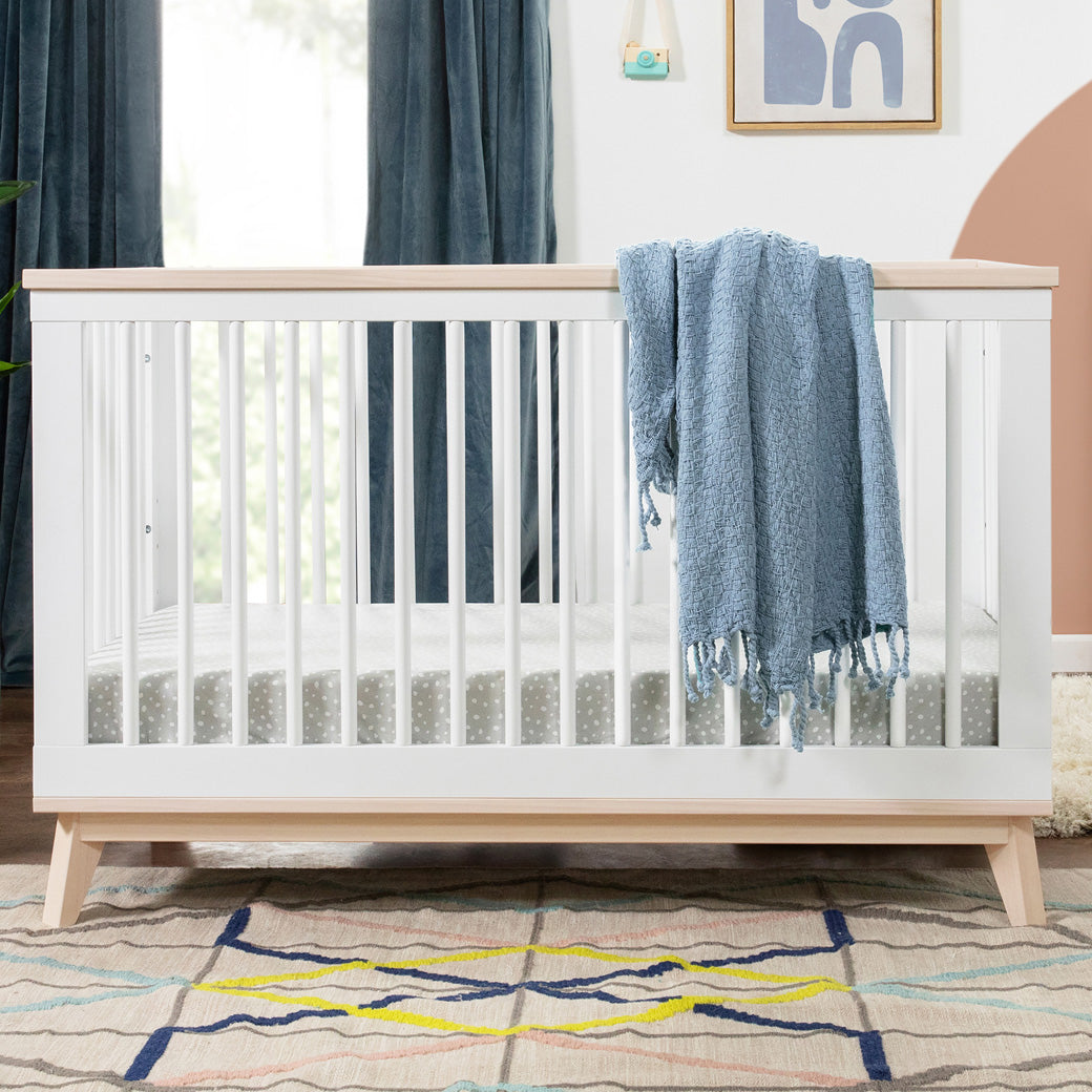 Babyletto's Scoot 3-in-1 Convertible Crib with a blanket over the rail in -- Color_Washed Natural/White