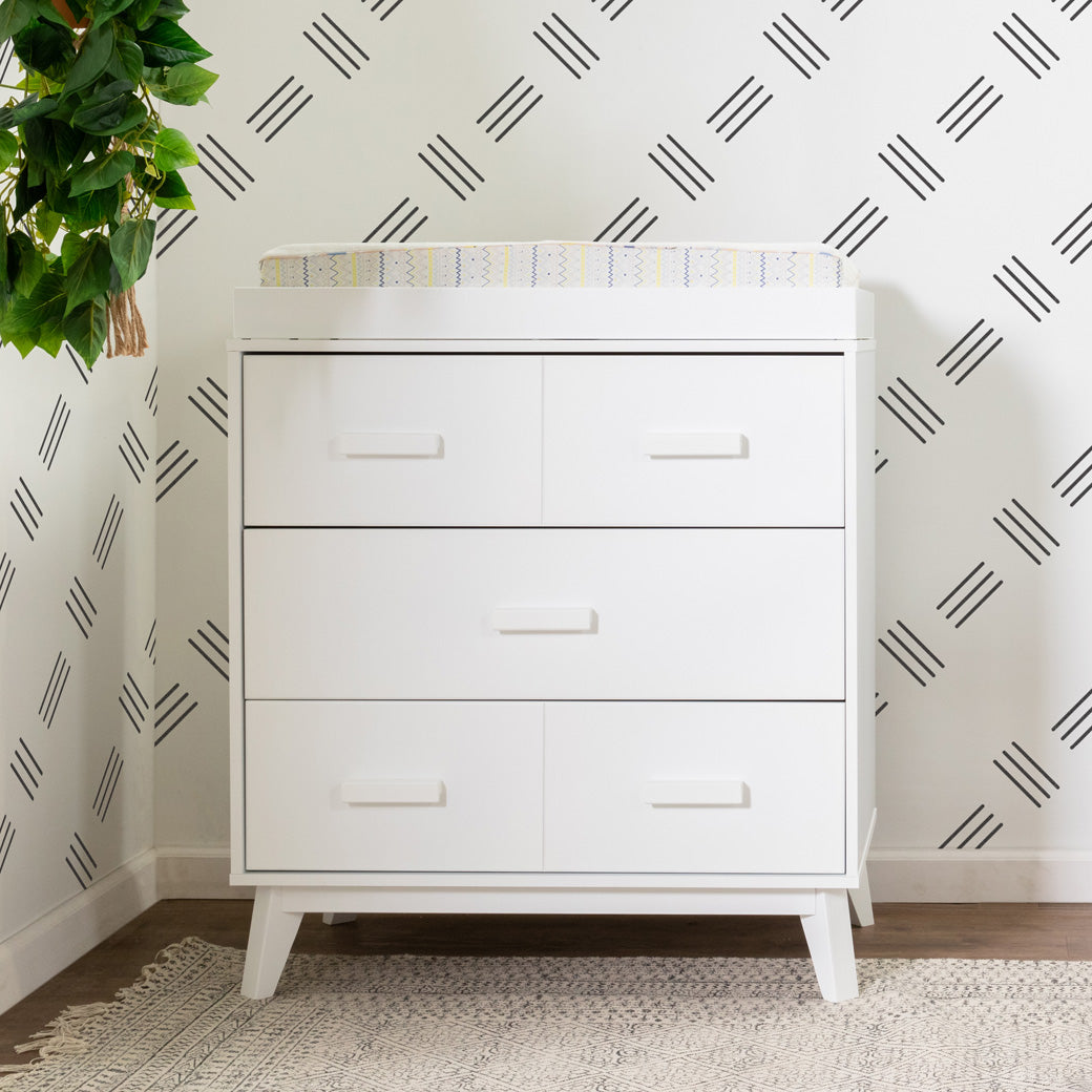 Babyletto's Scoot 3-Drawer Changer Dresser next to a plant with a changer  in -- Color_White