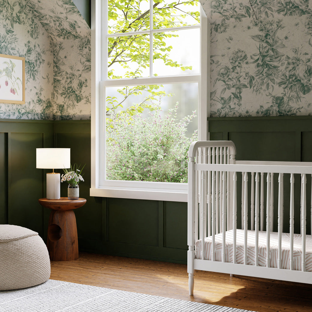 Lifestyle view of The Namesake Liberty 3-in-1 Convertible Spindle Crib in a green room, next to a window  in -- Color_Warm White