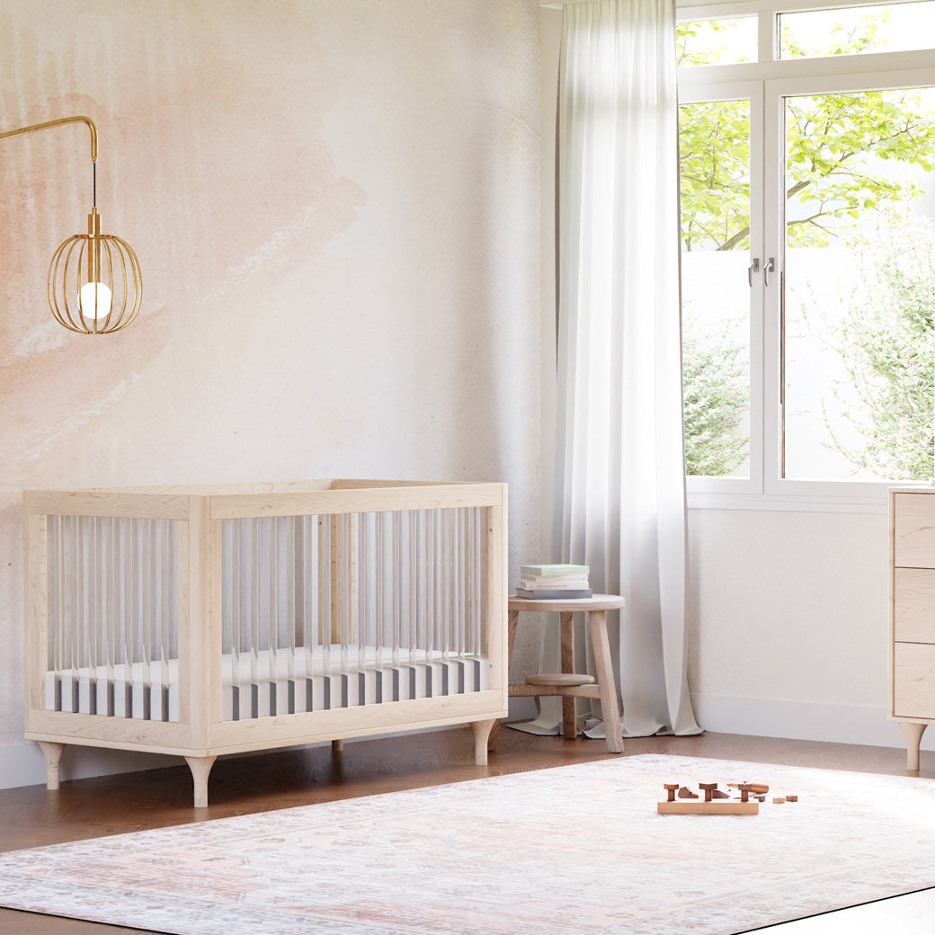 The Babyletto Lolly 3-in-1 Convertible Crib in a room next to a window in -- Color_Washed Natural / Acrylic