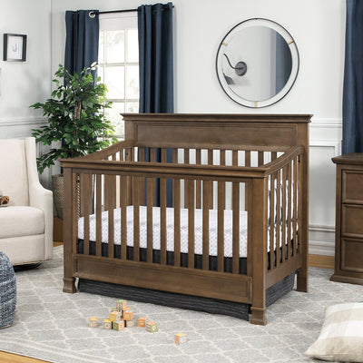 Namesake's Foothill 4-in-1 Convertible Crib in a nursery next to a recliner  in -- Color_Mocha