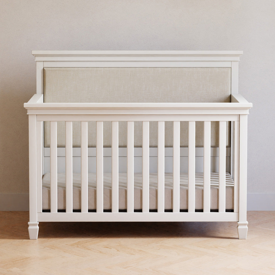 Darlington 4-in-1 Convertible Crib in Warm White front view, next to a wall