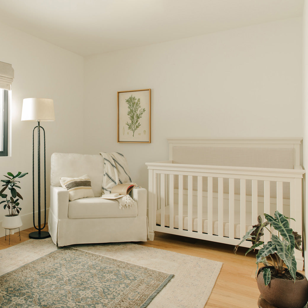 Darlington 4-in-1 Convertible Crib in Warm White in a room next to a recliner