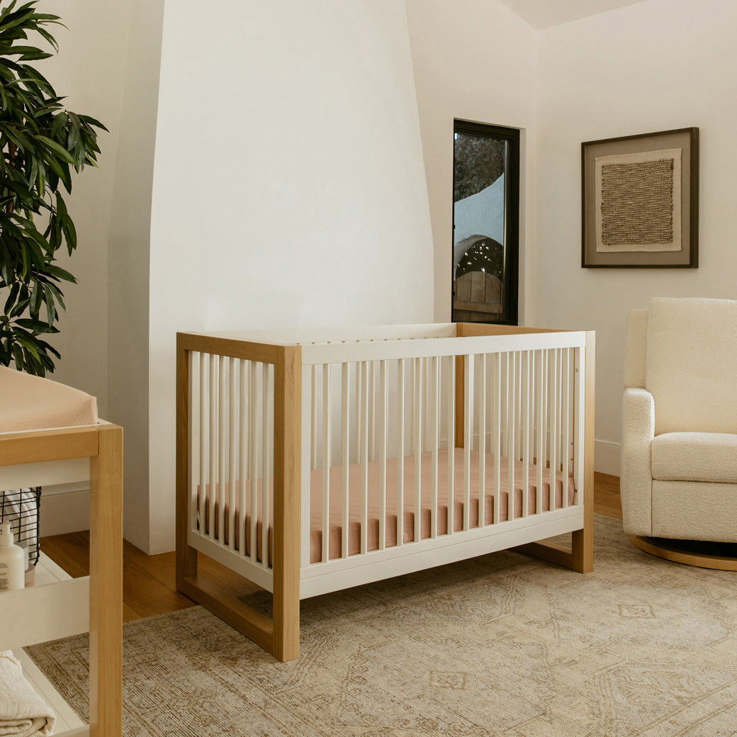 Namesake's Nantucket 3-in-1 Convertible Crib next to a recliner in -- Color_Warm White/Honey