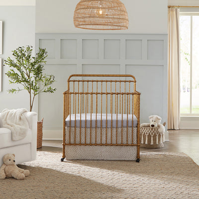 Namesake's Winston 4-in-1 Convertible Mini Crib next to a basket and recliner  in -- Color_Vintage Gold