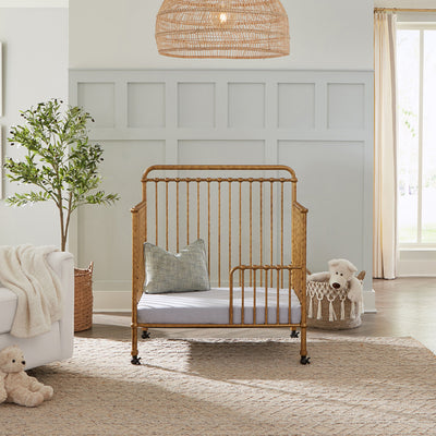 Namesake's Winston 4-in-1 Convertible Mini Crib as a toddler bed next to a basket and recliner  in -- Color_Vintage Gold