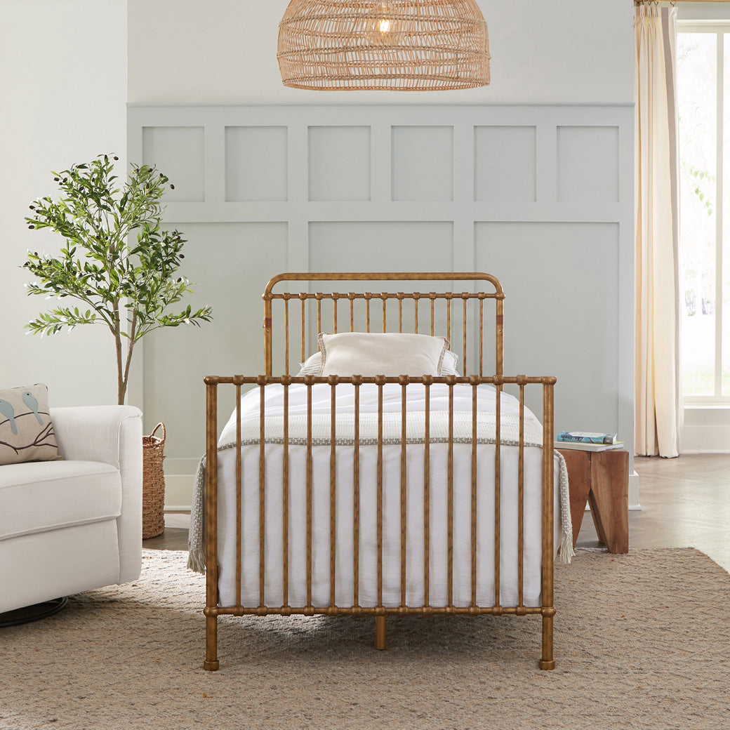 Namesake's Winston 4-in-1 Convertible Mini Crib as full-size bed next to a recliner and basket in -- Color_Vintage Gold