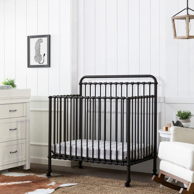 Namesake's Winston 4-in-1 Convertible Mini Crib next to a dresser and a recliner in -- Color_Vintage Iron