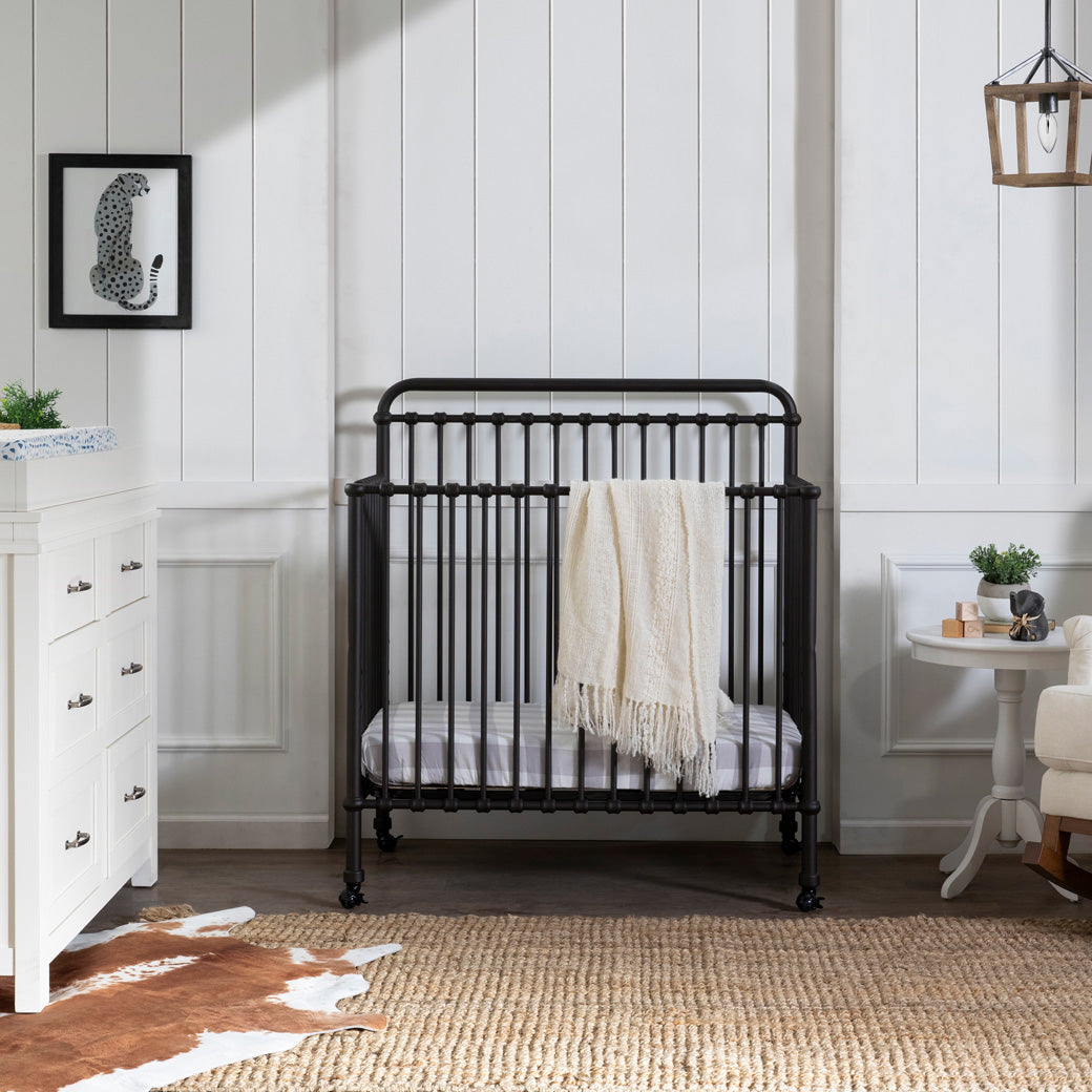 Namesake's Winston 4-in-1 Convertible Mini Crib next to a dresser in -- Color_Vintage Iron