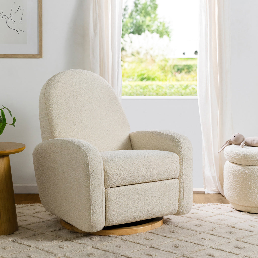 The Babyletto Nami Glider Recliner in a room next to a window in -- Color_Ivory Boucle With Light Wood Base