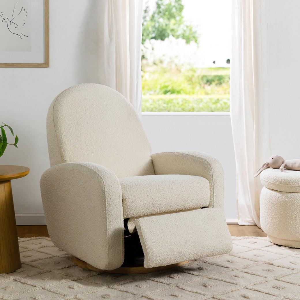 Semi-reclined footrest of The Babyletto Nami Glider Recliner in a room next to a window in -- Color_Ivory Boucle With Light Wood Base