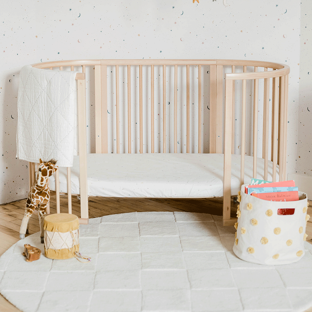 An empty toddler bed equipped with a Stokke's Sleepi V3 Fitted Sheet By Pehr in -- Color_Celestial