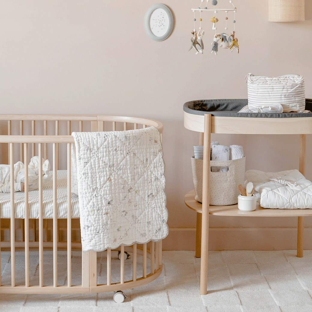 Stokke Sleepi Changer next to a crib equipped with the V3 Fitted Sheet by Pehr in -- Color_Stripes Away Pebbles