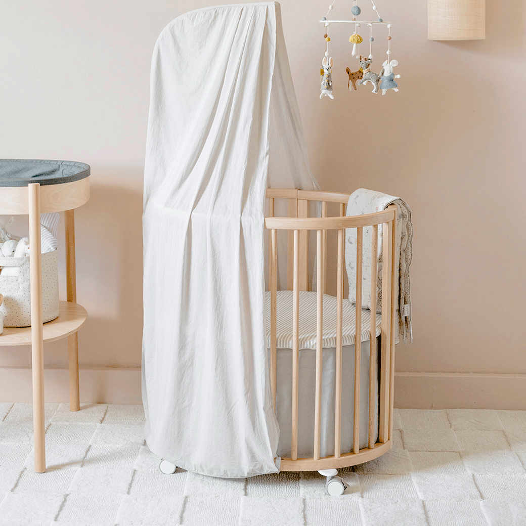 An empty crib equipped with The Stokke Sleepi V3 Mini Bed Skirt by Pehr in -- Color_Grey