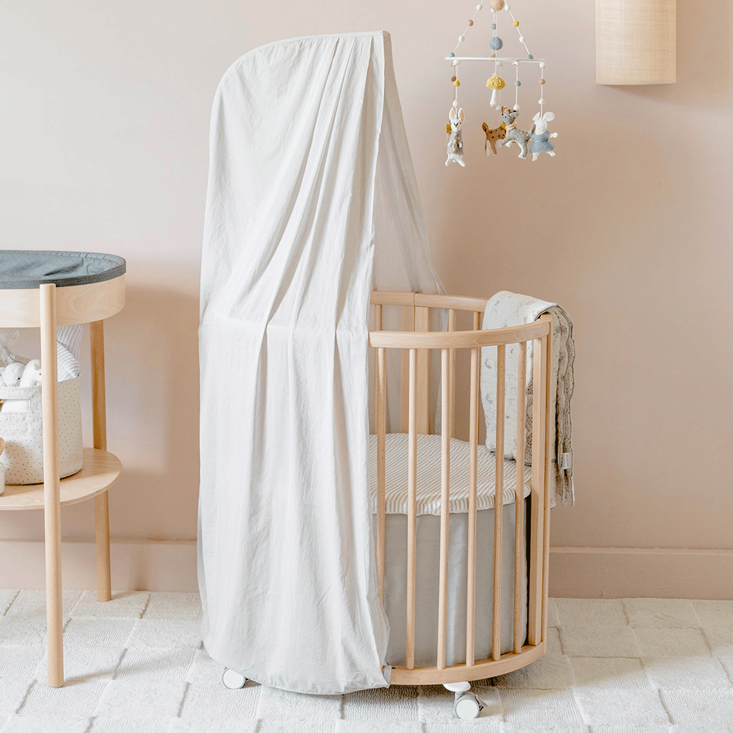 An empty crib equipped with a Stokke's  Sleepi V3 Mini Fitted Sheet By Pehr in -- Color_Stripes Away Pebbles