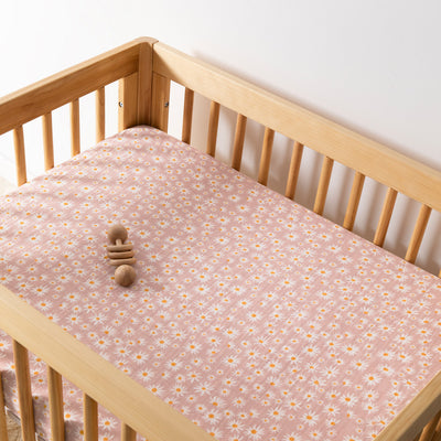 A crib with toy equipped with Babyletto's All-Stages Midi Crib Sheet In GOTS Certified Organic Muslin Cotton in -- Color_Daisy