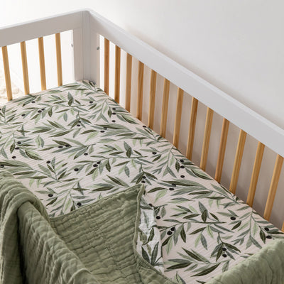 An empty crib with blanket equipped with the Babyletto's Crib Sheet in GOTS Certified Organic Muslin Cotton in -- Color_Olive Branches