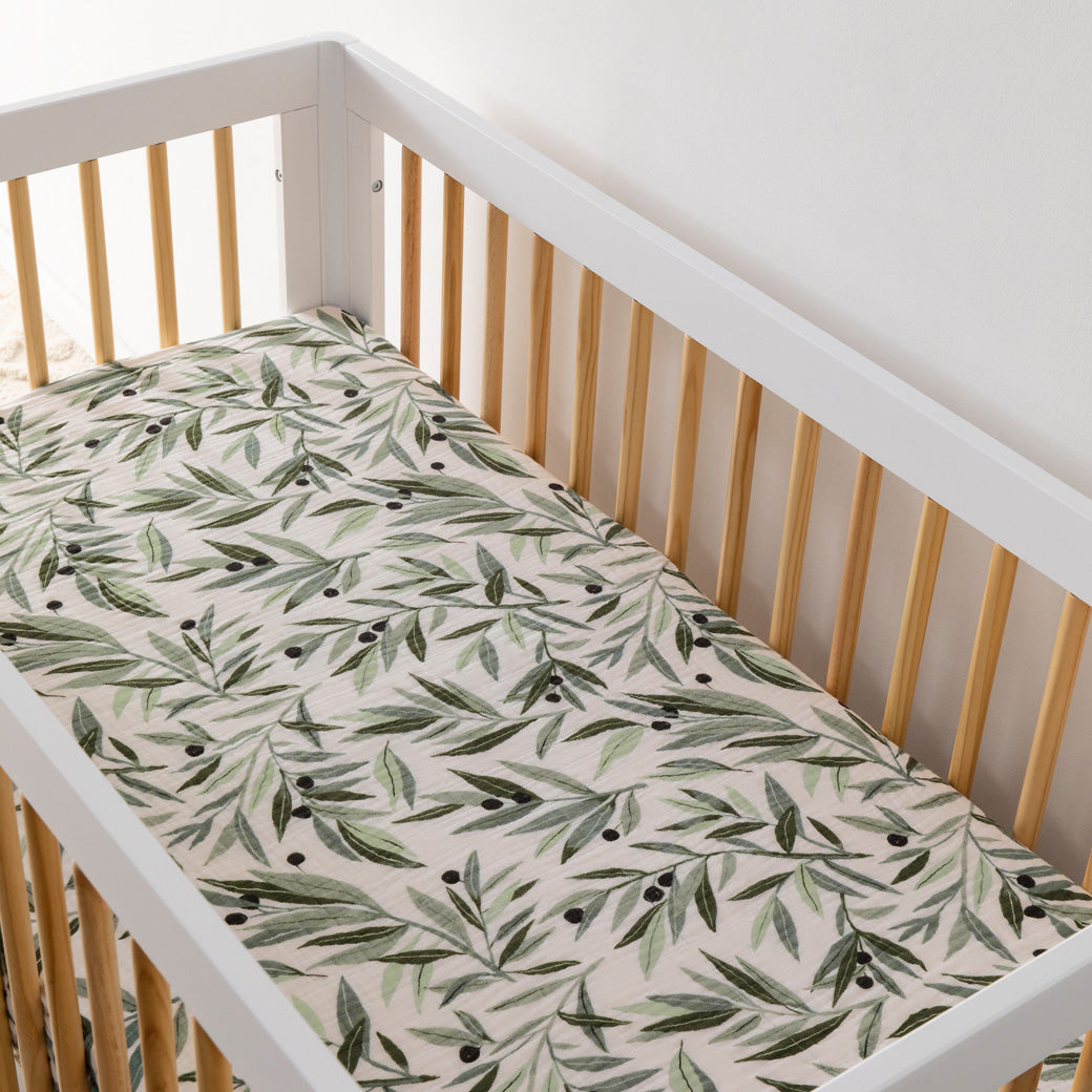 An empty crib equipped with the Babyletto's Crib Sheet in GOTS Certified Organic Muslin Cotton in -- Color_Olive Branches
