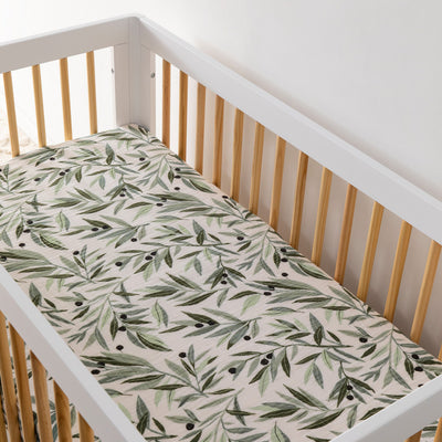 An empty crib equipped with the Babyletto's Crib Sheet in GOTS Certified Organic Muslin Cotton in -- Color_Olive Branches