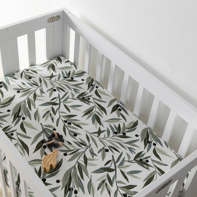 A crib with a toy inside  equipped with Babyletto's Mini Crib Sheet in -- Color_Olive Branches