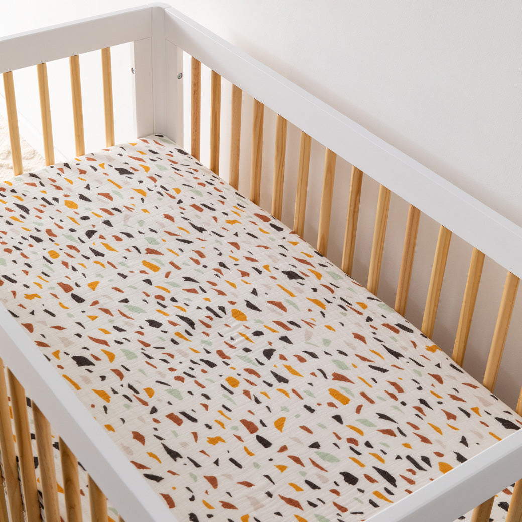 An empty crib equipped with the Babyletto's Crib Sheet in GOTS Certified Organic Muslin Cotton in -- Color_Terrazzo