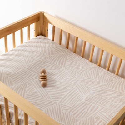 A crib with toy equipped with Babyletto's All-Stages Midi Crib Sheet In GOTS Certified Organic Muslin Cotton in -- Color_Oat Stripe