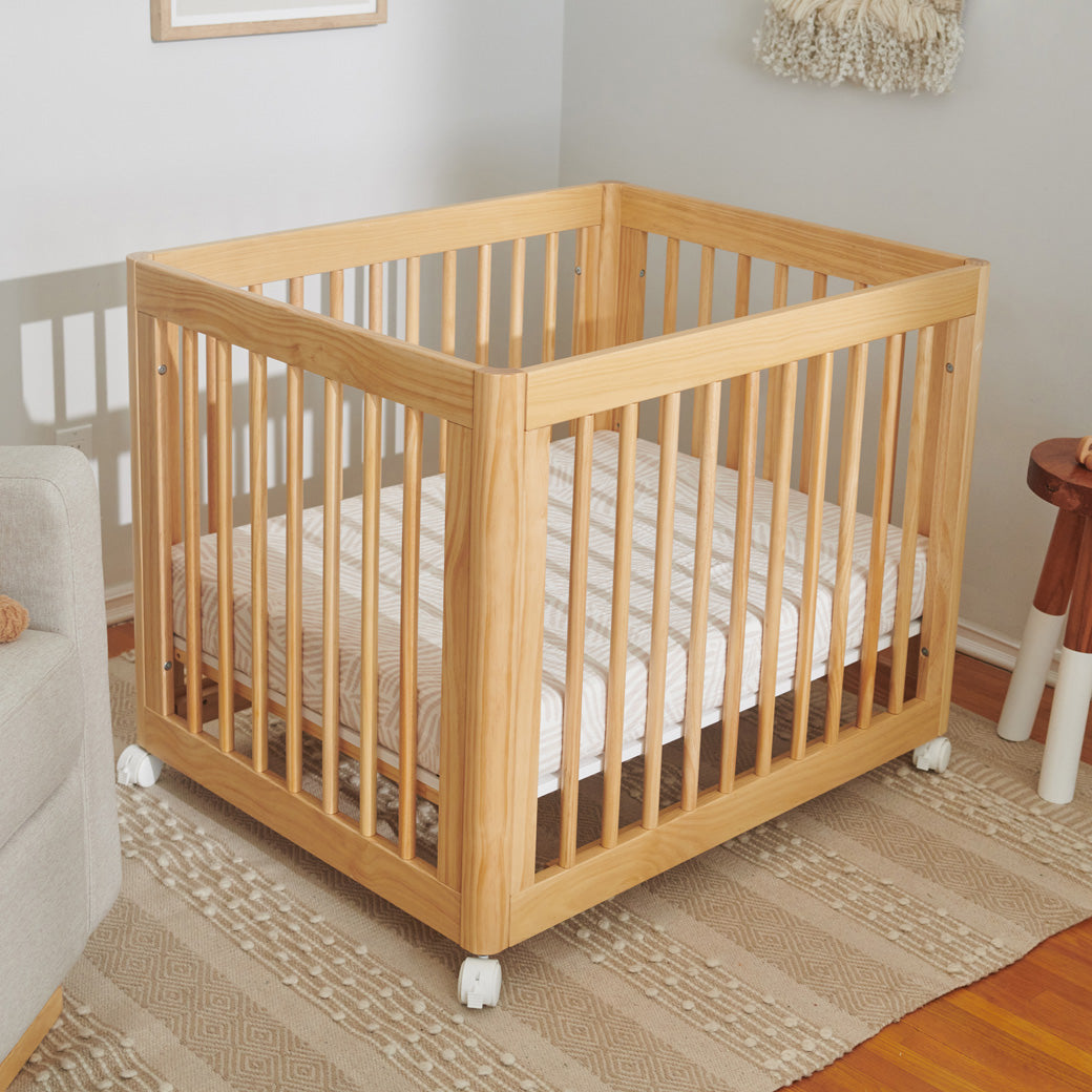 A crib  equipped with Babyletto's All-Stages Midi Crib Sheet In GOTS Certified Organic Muslin Cotton in -- Color_Oat Stripe