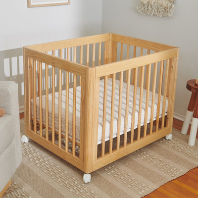 A crib  equipped with Babyletto's All-Stages Midi Crib Sheet In GOTS Certified Organic Muslin Cotton in -- Color_Oat Stripe