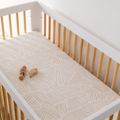 A crib with toy equipped with the Babyletto's Crib Sheet in GOTS Certified Organic Muslin Cotton in -- Color_Oat Stripe
