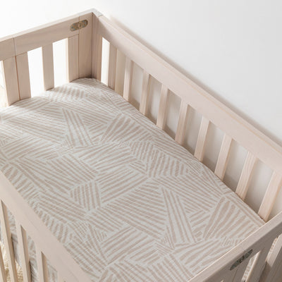 Empty crib equipped with Babyletto's Mini Crib Sheet in -- Color_Oat Stripe