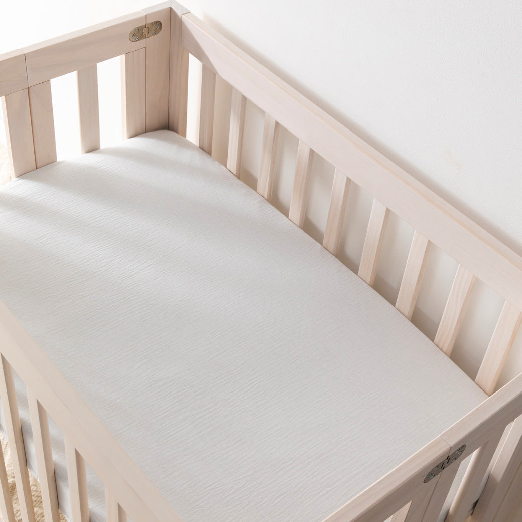 Empty crib equipped with Babyletto's Mini Crib Sheet in -- Color_White