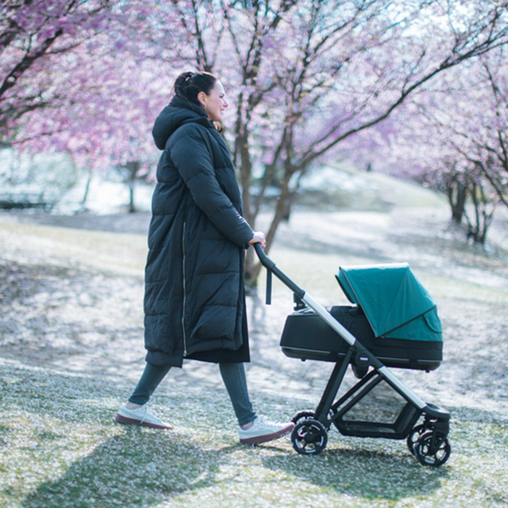 Side view of a young woman wrapped up in warm clothing on a cold day pushing the Thule Shine Stroller in -- Color_Mallard Green