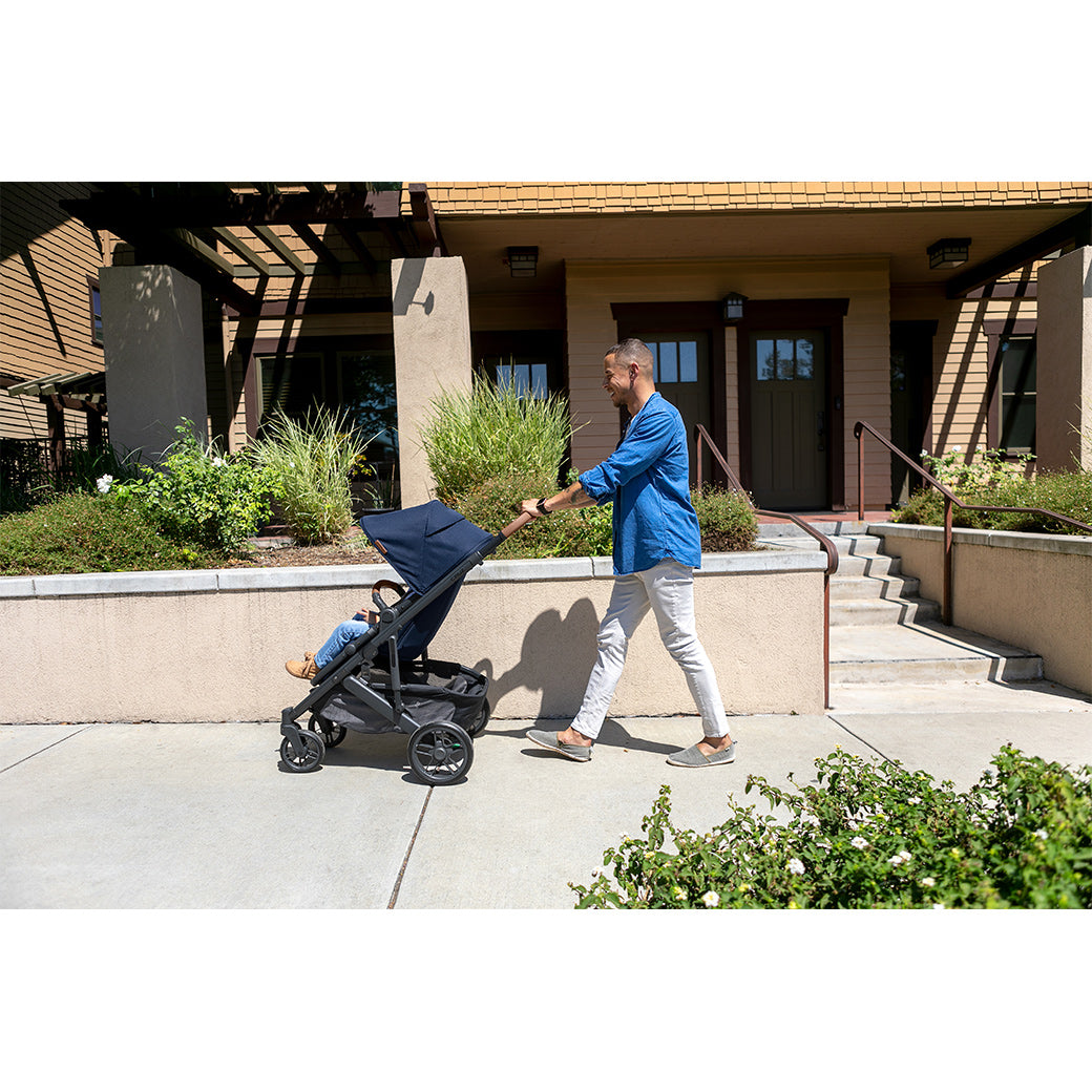 Dad in front of a house pushing a toddler in the UPPAbaby CRUZ V2 Stroller in -- Color_Noa