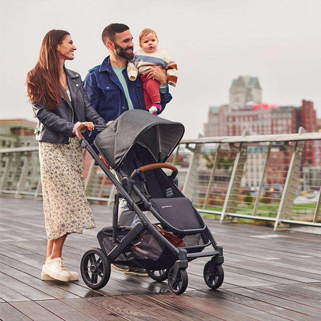 Dad holding a baby and mom pushing the UPPAbaby Cruz V2 Stroller in -- Color_Gregory