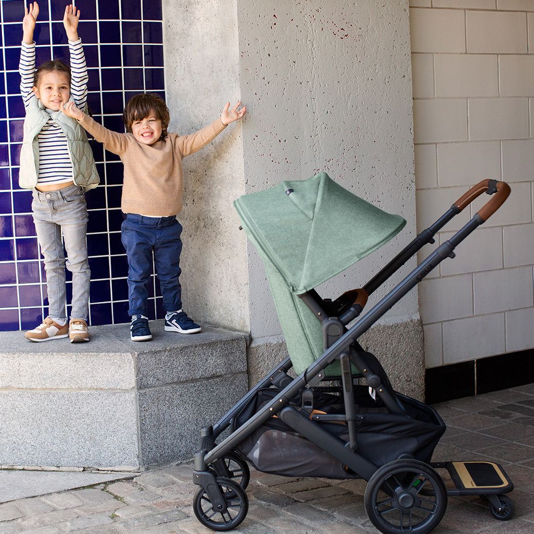 Two kids smiling and standing next to CRUZ V2 Stroller in color gwen -- Color_Gwen