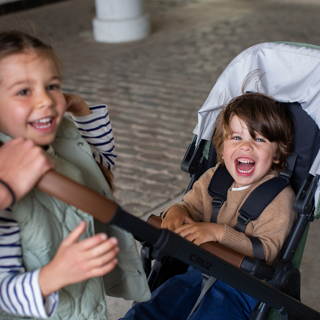 A child smiling next to the stroller and another sitting in the CRUZ V2 stroller -- Color_Gwen