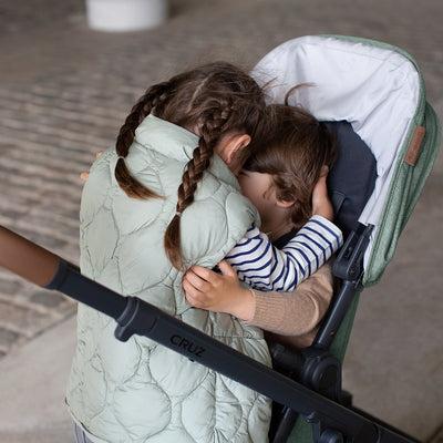 A child hugging her sibling that is sitting in the UPPAbaby Cruz V2 Stroller in -- Color_Gwen