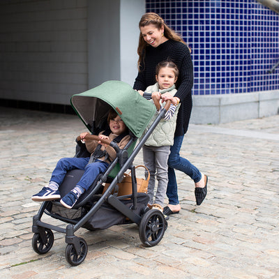 A mom with her two kids walking down the street and pushing the UPPAbaby Cruz V2 Stroller in -- Color_Gwen