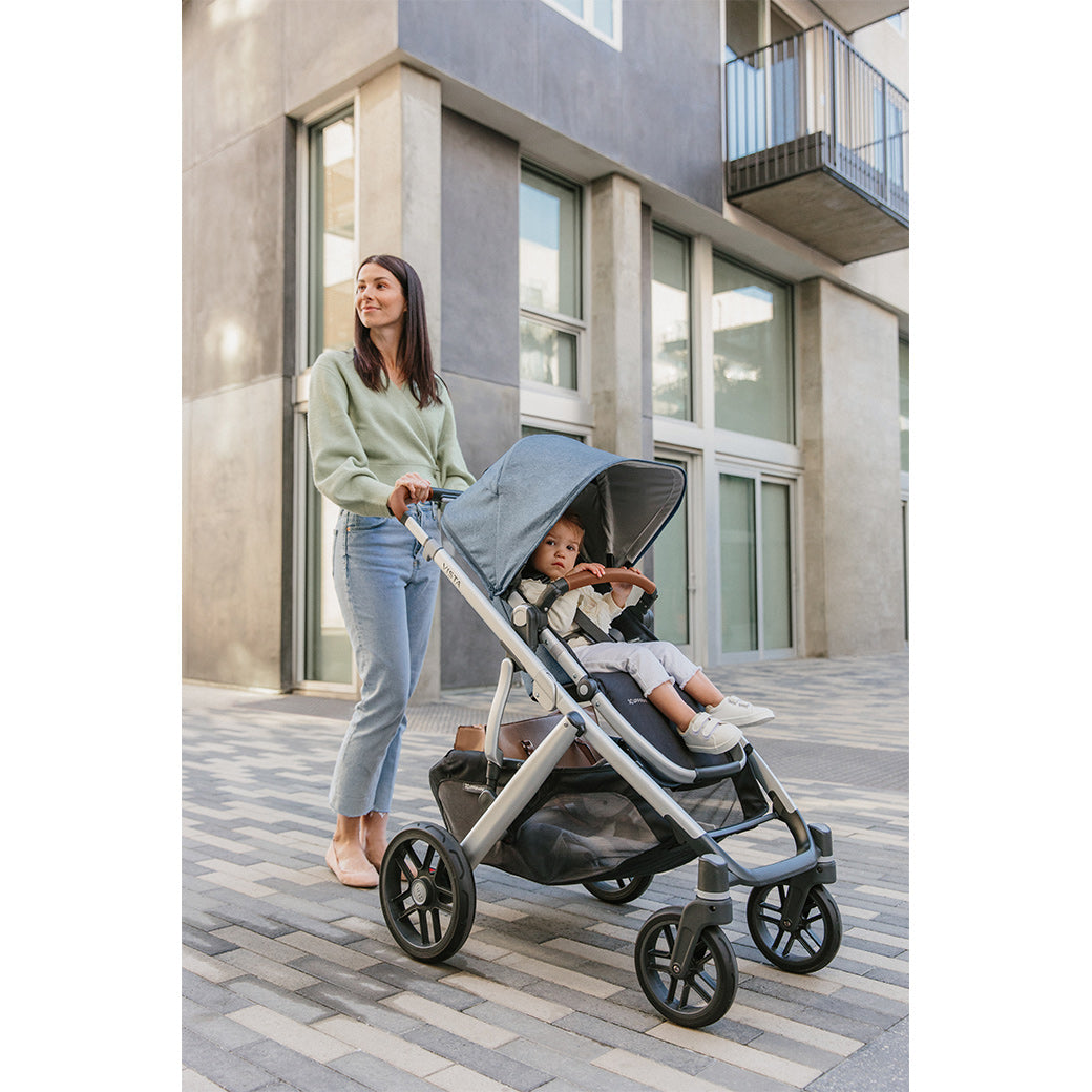 Mom pushing a baby down the street in the UPPAbaby VISTA V2 Stroller in -- Color_Gregory