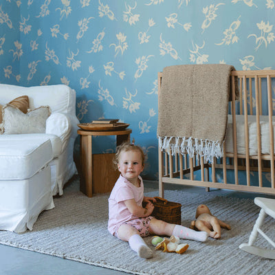 A child sitting next to a crib in a room furnished with Anewall After The Rain Floral Mural